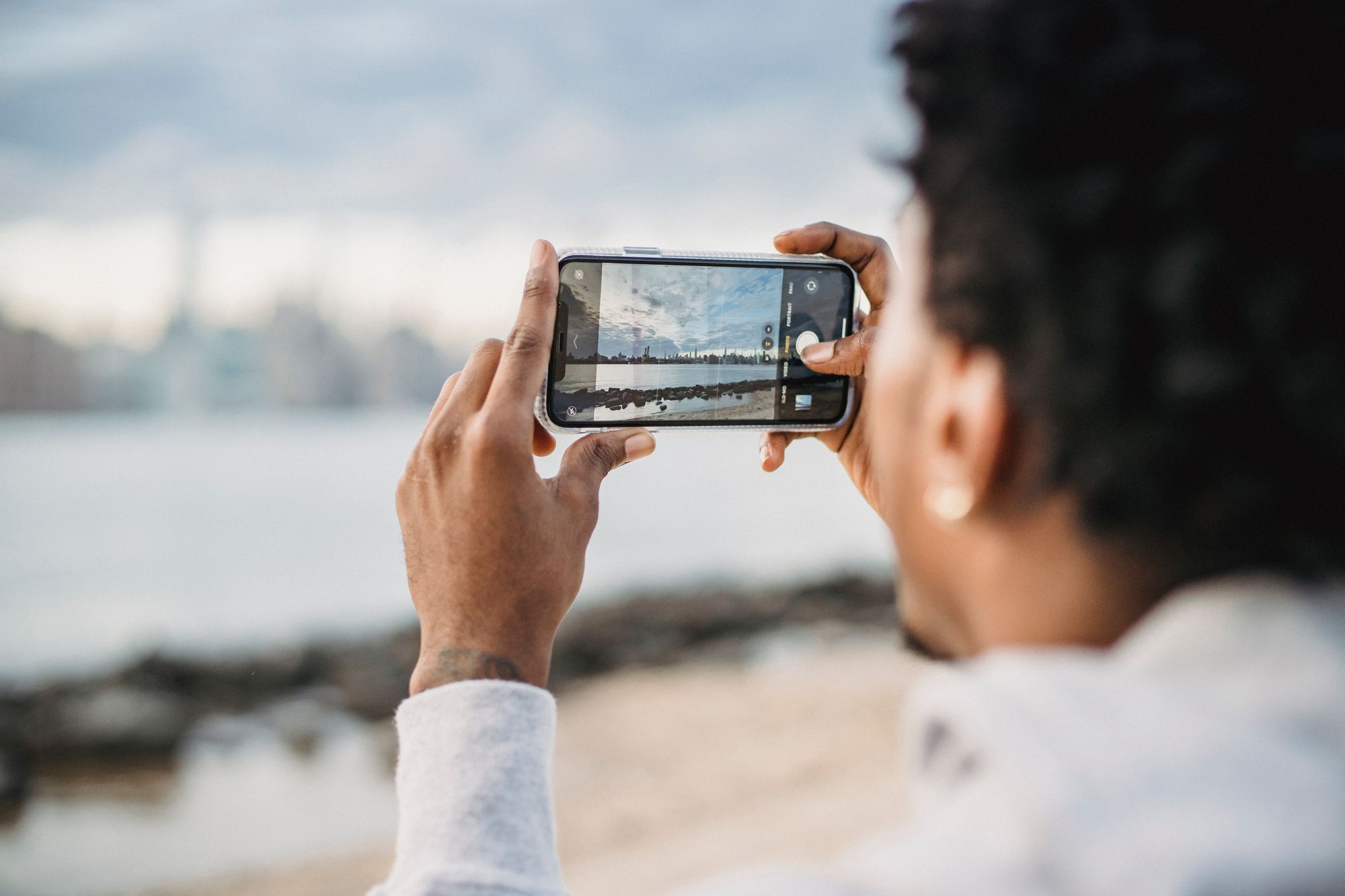 Une personne photographie un paysage avec son téléphone, vue de dos.