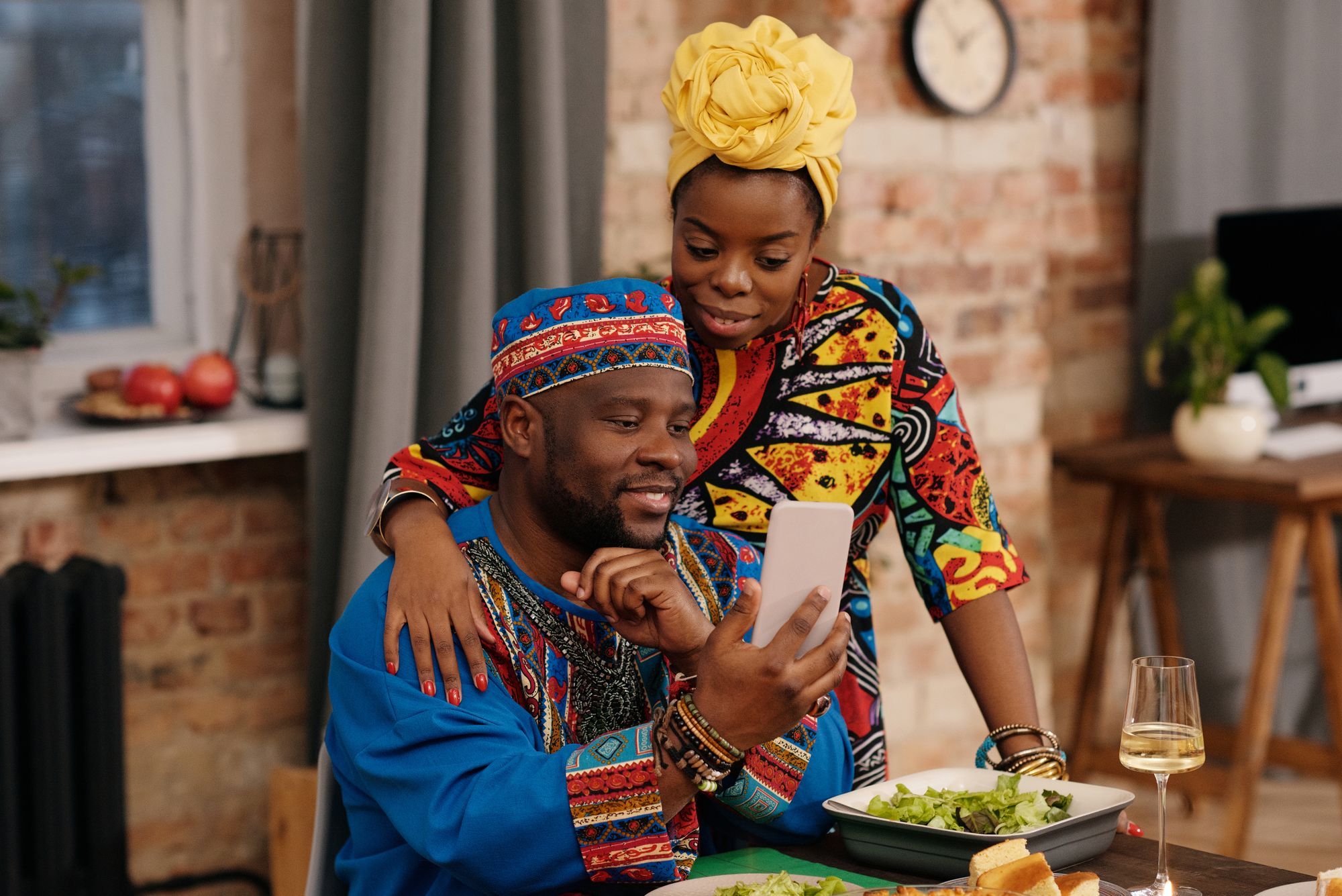 Un couple en tenue colorée regarde ensemble l'écran d'un téléphone, chez lui.
